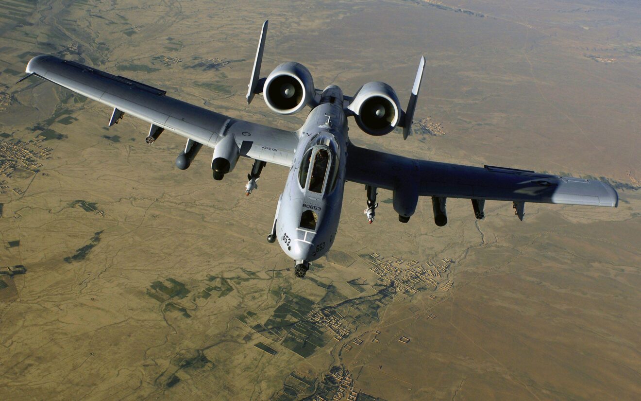 A-10 Thunderbolt II, commonly known as the "Warthog," in flight over a desert landscape, showcasing its distinctive twin engines, straight wings, and powerful GAU-8 Avenger rotary cannon designed for close air support missions.