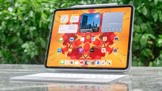 iPad with keyboard and Apple Pencil, displaying colorful home screen outdoors.