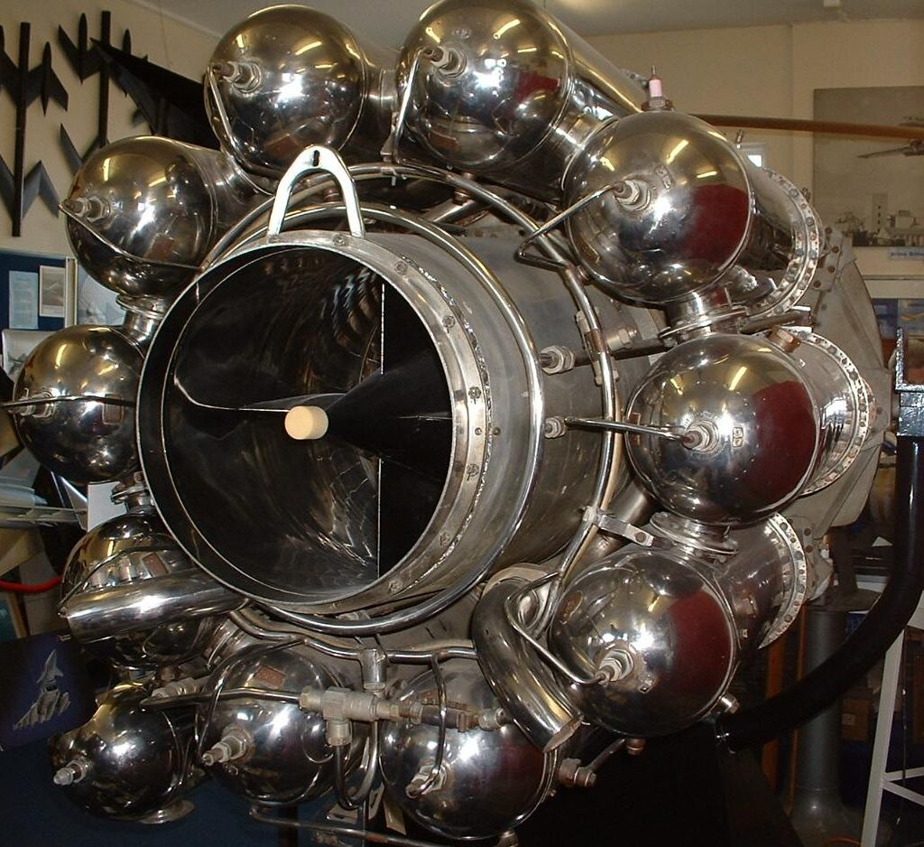 Close-up image of the Whittle W.2/700 jet engine, showcasing its circular array of polished combustion chambers and central intake cone, displayed in a museum setting.